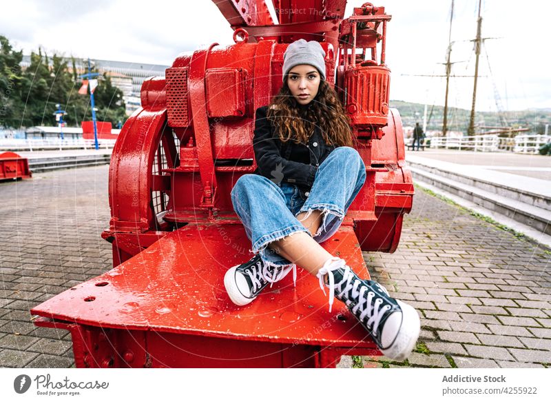 Woman in jeans and warm clothes resting on metal construction woman confident outerwear urban contemplate cool female young modern calm casual trendy denim