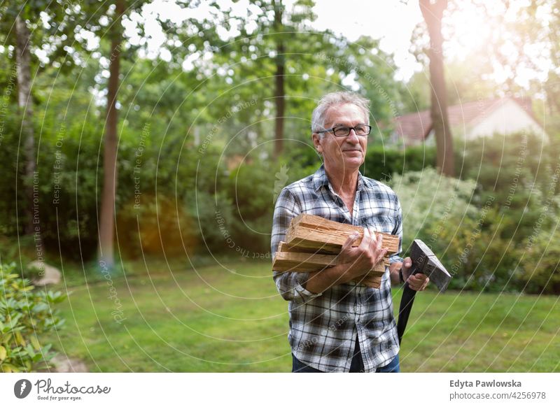 Senior man cutting logs, working in the garden senior old men male home house people lifestyle enjoying at home domestic life real people pensioner pensioners