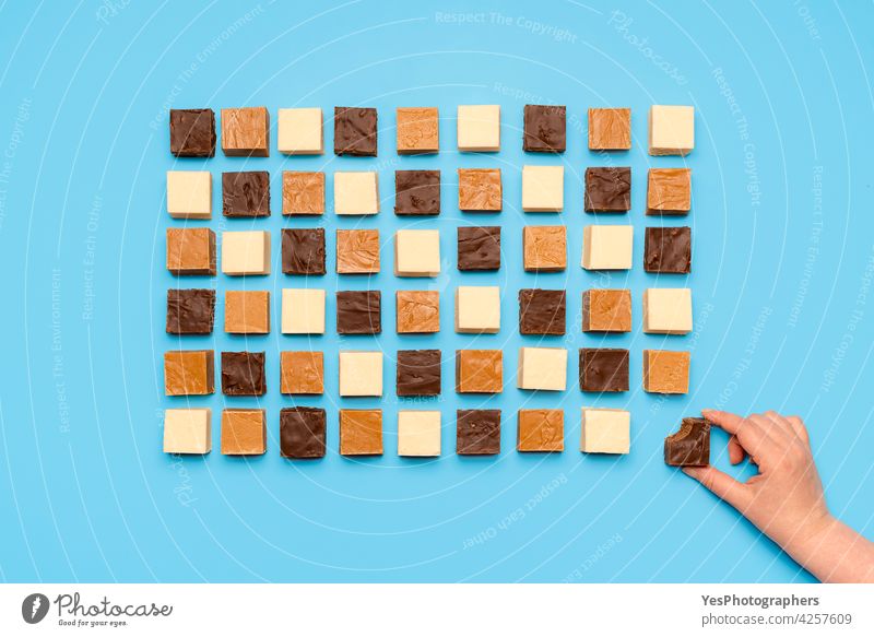 Fudge assortment aligned symmetric on blue table. Woman grabbing chocolate fudge, top view above abundance american background bite brown candy caramel