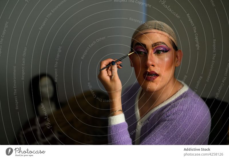 Feminine man applying makeup in dressing room androgynous feminine drag queen queer visage eccentric cosmetic individuality style extravagant prepare brush