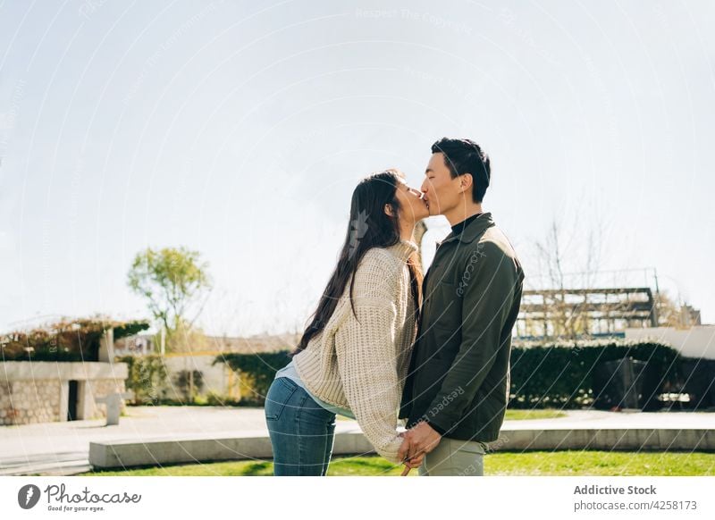 Romantic young Asian couple holding hands and kissing in park love relationship bonding romantic date together happy affection city positive boyfriend