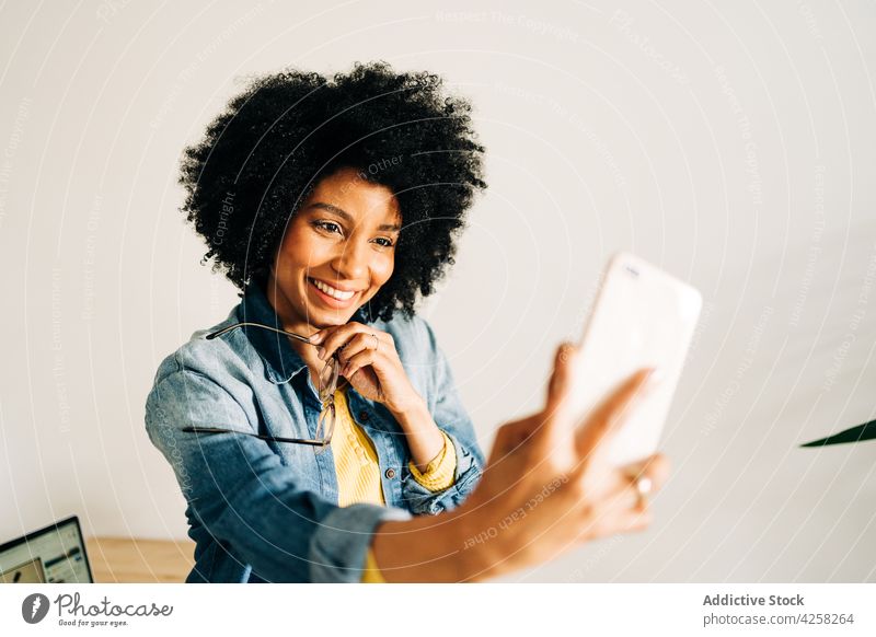 Happy black woman in eyeglasses smiling and taking selfie happy smile positive smartphone mobile carefree female yellow sweater self portrait joy afro hairstyle