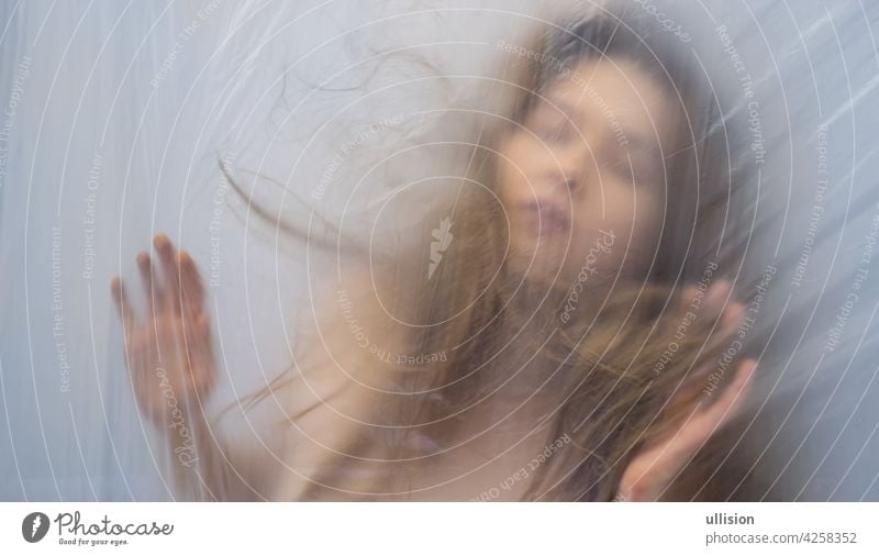 Blurred, out of focus portrait of beautiful sexy sensual seductive woman behind plastic foil like in a dream as background, copy space transparent demoniac