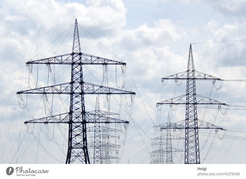 Power lines - many power poles one after the other and side by side in front of a cloudy sky stream power supply power line Electricity pylon Many Energy