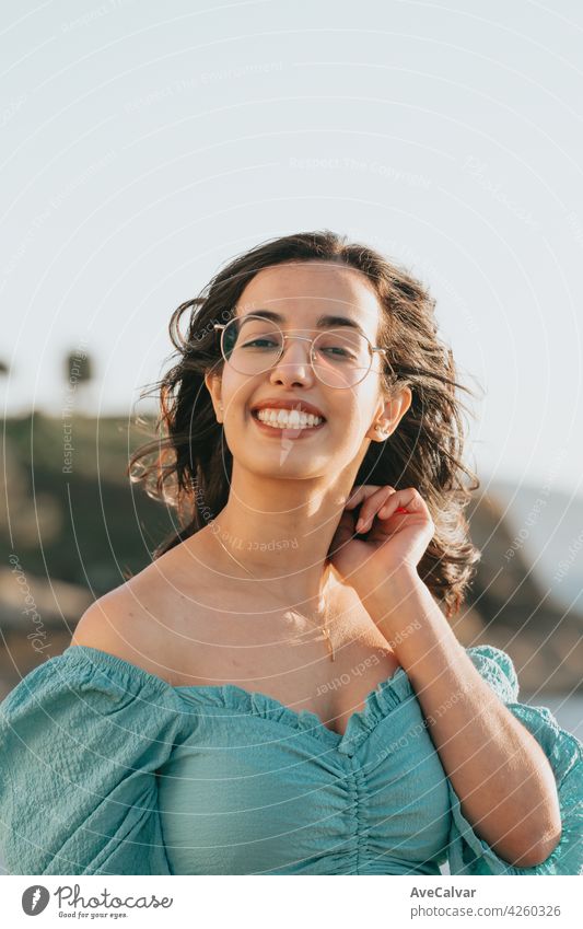 Young woman with glasses smiling to camera during a super sunny day with copy space lifestyle concept happy day person carefree enjoying face fun hair