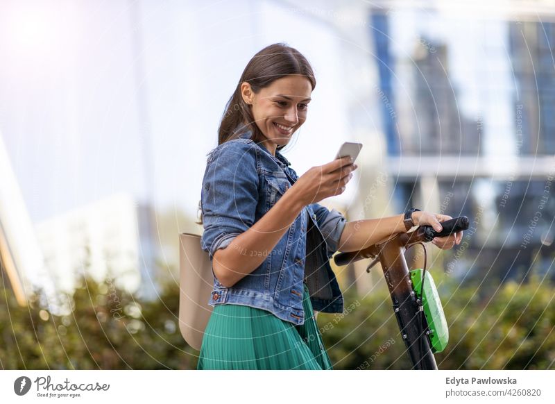 Activating electric scooter from smart phone urban street city active people woman young adult casual attractive female happy Caucasian enjoying one person