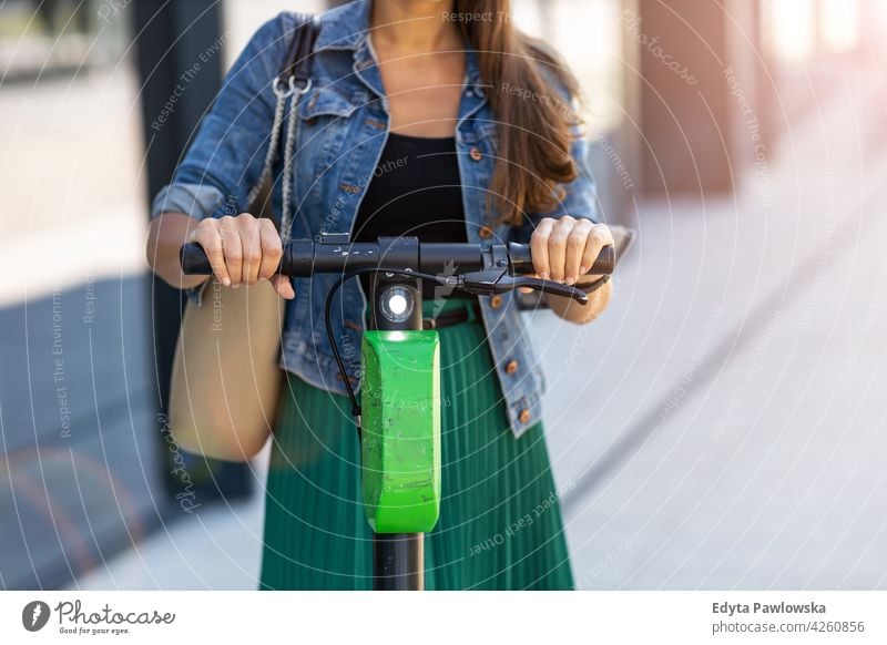 Female commuter riding electric push scooter urban street city active people woman young adult casual attractive female happy Caucasian enjoying one person