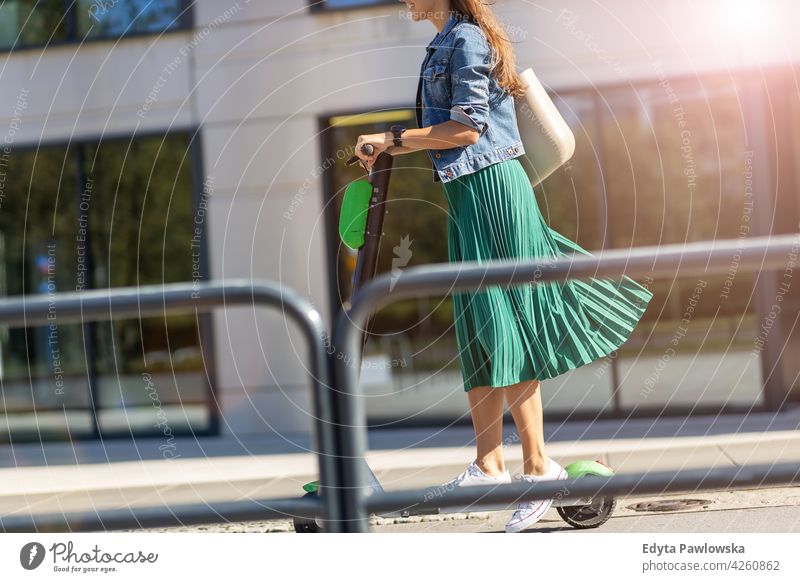 Female commuter riding electric push scooter urban street city active people woman young adult casual attractive female happy Caucasian enjoying one person