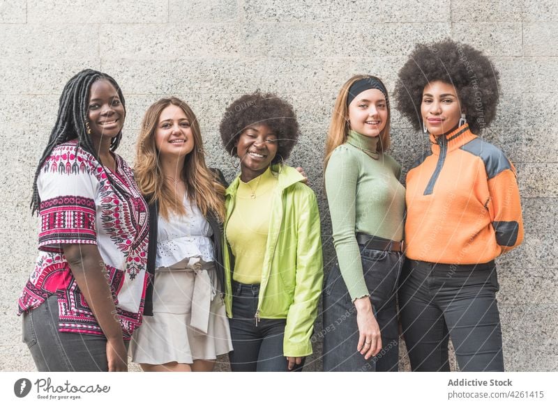 Confident multiracial girlfriends in casual wear against wall self assured happy street style fashion smile individuality vain friendship feminine millennial