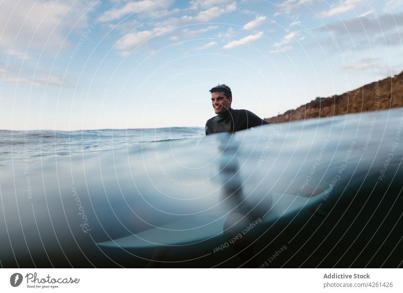 Smiling sportsman practicing surfing in ocean under cloudy sky surfer surfboard smile mount nature sea water wavy ripple wellness vitality endless horizon