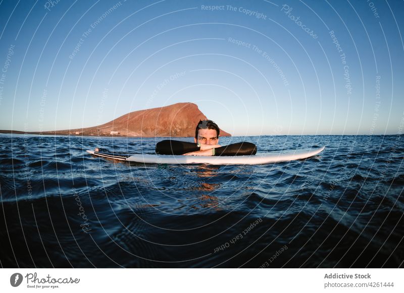 Smiling sportsman practicing surfing in ocean under cloudy sky surfer surfboard smile mount nature sea water wavy ripple wellness vitality endless horizon blur