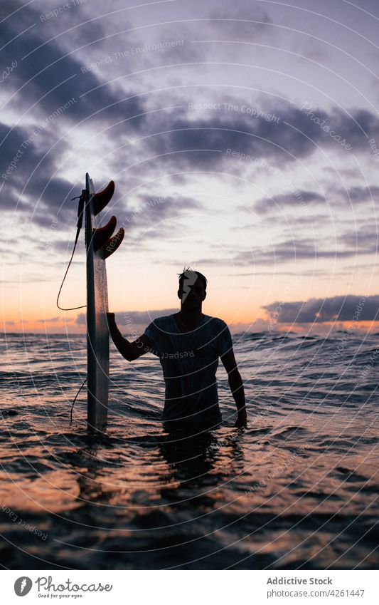 Anonymous surfer with surfboard in sea at sundown sportsman ocean silhouette nature seascape cloudy sky equipment professional atmosphere air fluffy wavy admire