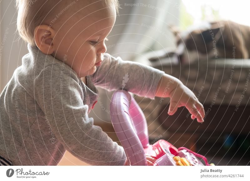 Toddler playing with walker push toy; leaning on toy while standing and reaching for interactive button toddler learning step balance baby child milestone