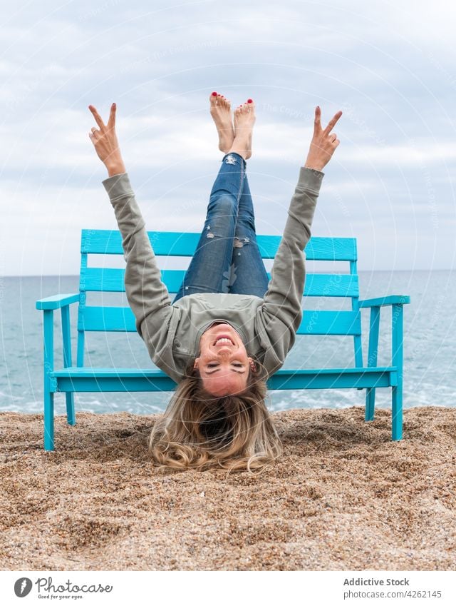 Smiling woman having fun on bench against sea two fingers legs crossed cheerful weekend peace legs raised seashore sky ocean coast sandy beach seaside enjoy