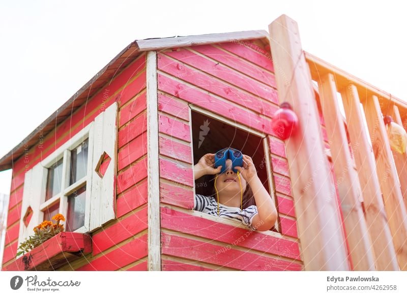 Boy in a wooden playhouse looking through a binocular binoculars holding adventure exploration red Sweden tree tree house treehouse summer outdoors playful