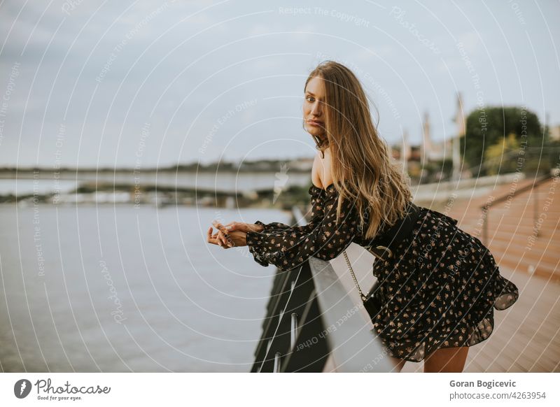 Young long hair brunette woman standing on the riverside alone attractive bag beautiful beauty broad caucasian city day dress elegant fashion female hairstyle