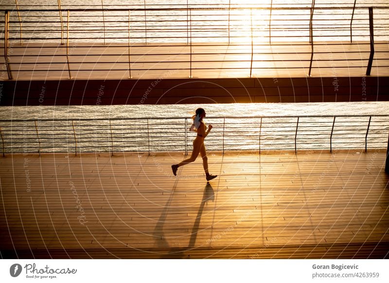 Young woman taking running exercise by the river promenade young jogging yellow training athlete people lifestyle healthy person adult sport activity city