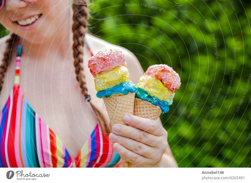 Beautiful girl holding two colorful ice cream with sprinkles wearing a rainbow colored swimsuit in the summer, pink sunglasses and braids happy vacation,holidays concept