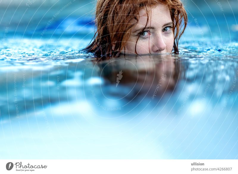 Portrait of young sexy woman with red hair, redhead swimming in the pool, head half submerged under water, copy space wet summertime enjoyment attractive