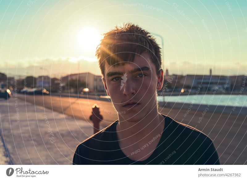 portrait of a serious teenager with the sun behind his head young man sad worried tired sunset harbor pier backlit sunlight evening street outdoors beautiful