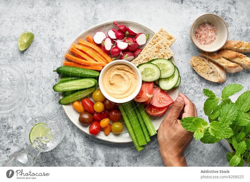 Plated of assorted healthy fresh vegetables with hummus served on table near bread person healthy food cucumber tomato carrot radish spinach colorful vegetarian