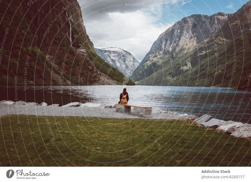 Tourist sitting on bench on shore of mountain lake traveler admire highland slope ridge discovery range trip person freedom nature tourism journey explore