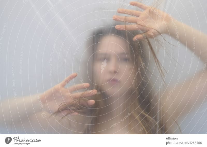 fantastic outstanding strange portrait with protective defensive hands in anxiety dream of beautiful sexy sensual woman behind transparent plastic foil as background, copy space