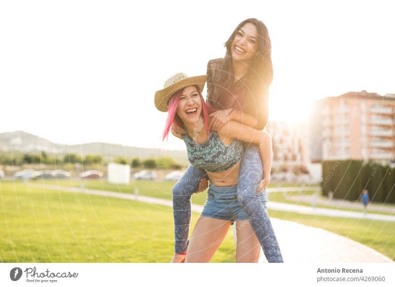 Two playful woman playing in park in sunset light young attractive 20s joy people person youth urban women pretty pretty people outdoors city carrying happy