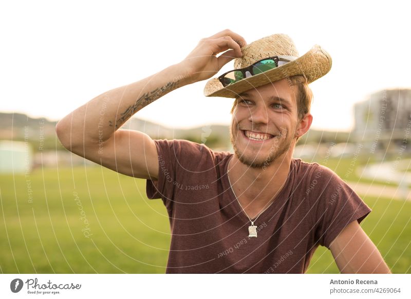 A young blond man adjusts a hat at sunset attractive 20s joy people person youth urban pretty pretty people outdoors city men ht blonde sunglasses park summer