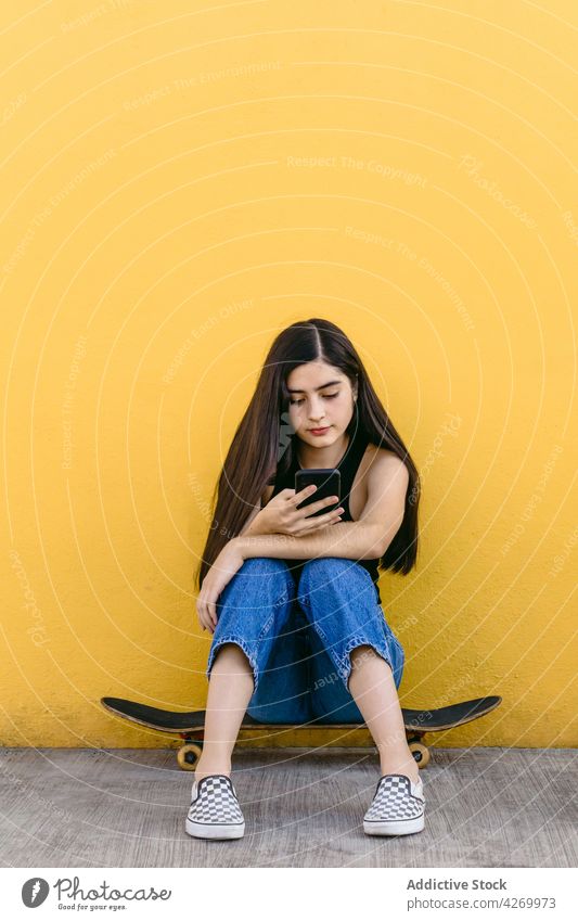 Skateboarder chatting on smartphone on pavement on yellow background skater internet online skateboard social media adolescent using gadget device cellphone