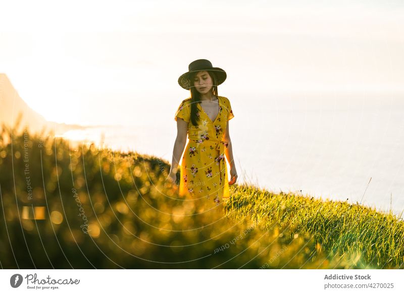 Young woman standing on grass lawn sundress countryside nature dreamy grassland meadow grassy young field hat appearance serene grace feminine carefree peaceful