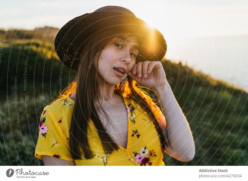 Young woman standing on grass lawn sundress countryside nature dreamy grassland meadow grassy young field hat appearance serene grace feminine carefree peaceful