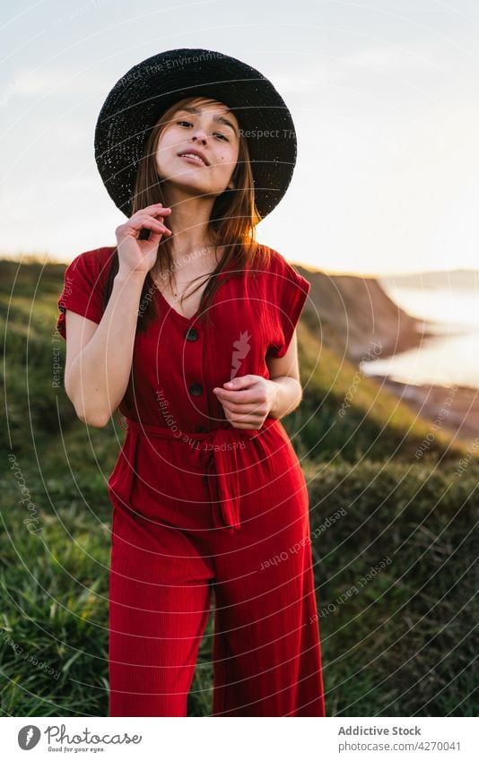 Young woman standing on grass lawn sundress countryside nature dreamy red grassland meadow grassy young field hat appearance serene grace feminine carefree