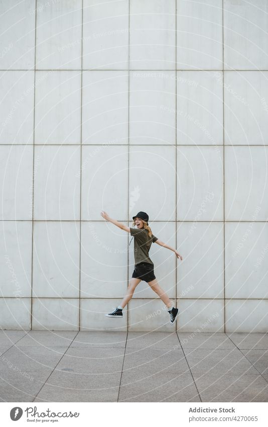 Happy woman jumping over urban pavement against wall outstretch happy active having fun energy dynamic lifestyle city tile cheerful gumshoe modern stroll