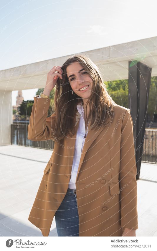 Smiling female on walkway on station near constructions on street woman happy pavement alone elegant blue sky smile young trendy sunlight confident jeans beam