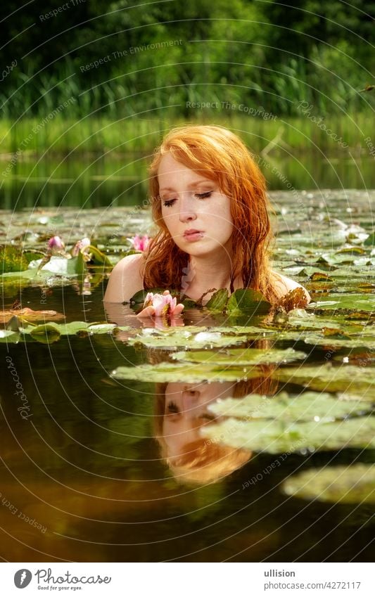 Delicate young sexy red-haired woman enjoys sensually seductive sensual in the water, pond, on a pink water lily flower. Portrait Red hair Pond River Lake