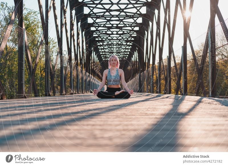 Woman meditating in Lotus pose on bridge in sunshine woman lotus pose meditate yoga spirit stress relief energy harmony mudra footpath eyes closed idyllic