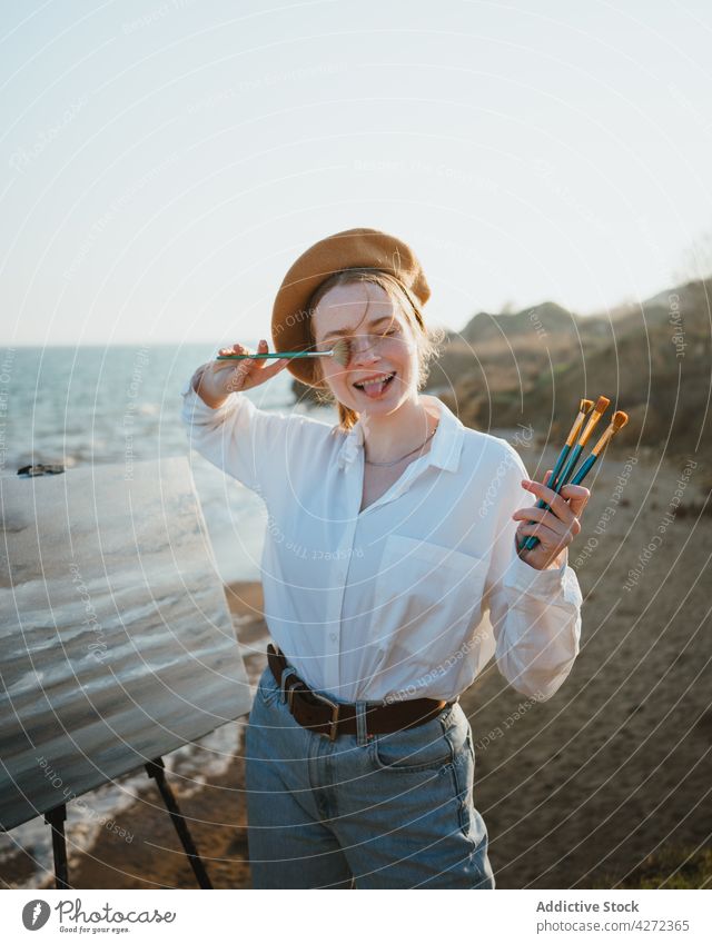 Lady painter on coast near sand and ocean and painting woman beach hobby artist paintbrush grimace artwork female young draw daytime sky easel lonely alone