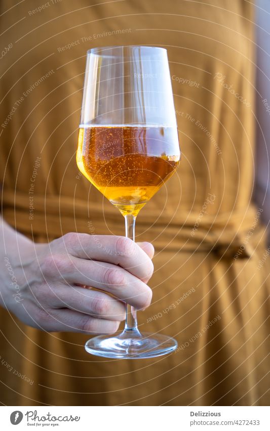 A woman in an orange dress holding a glass of cider, close-up of a summer drink alcohol apple apple cider french photography female hand outdoors outside sun