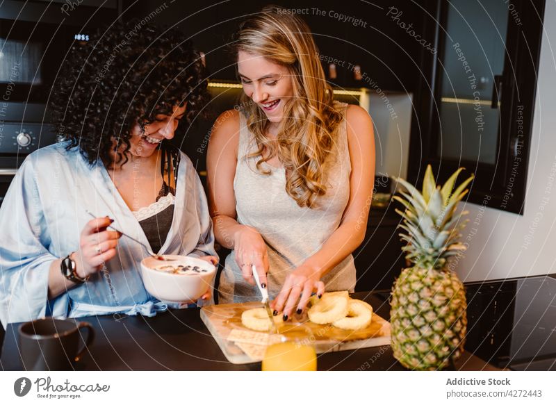 Happy girlfriends having fun in morning in kitchen women couple laugh cut pineapple joy breakfast lgbt cereal female pleasure lesbian cheerful happy berry