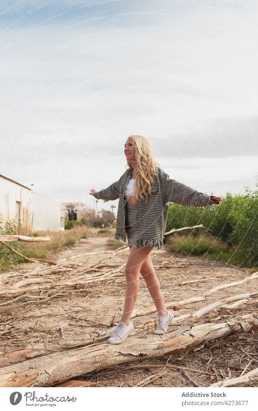 Young smiling woman outstretching arms while balancing on log balance positive tiptoe countryside nature rural pleasure posture female optimist smile casual