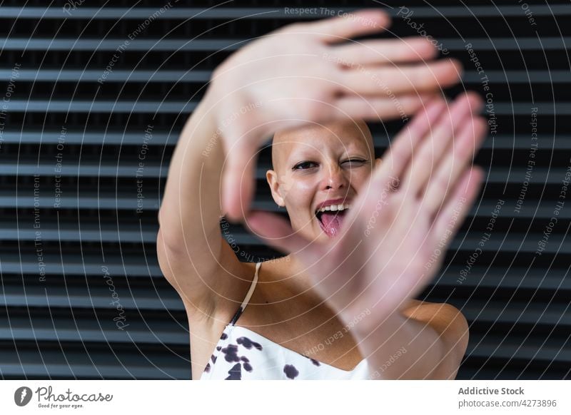 Positive young bald woman showing camera and smiling gesture smile positive alopecia tongue out trendy individuality delight style glad street female outfit