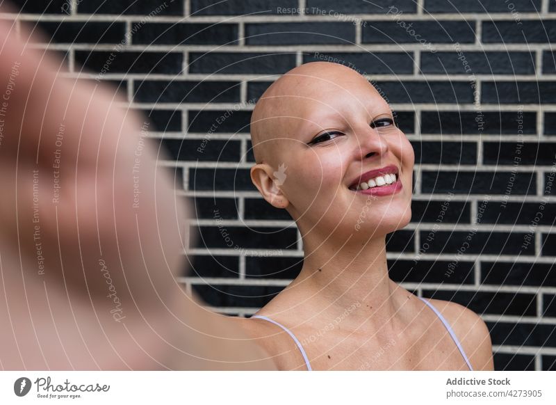 Smiling bald woman taking selfie on phone near brick wall smartphone smile street modern happy female young device mobile gadget using lifestyle city urban