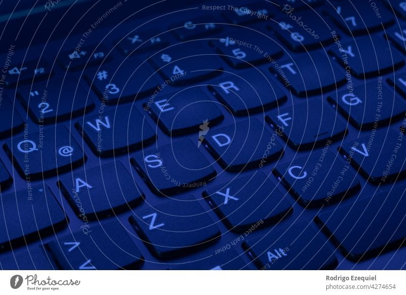 QWERTY Keys of a laptop computer keyboard illuminated with uv ultraviolet purple light background black blue business button concept dark darkened room data