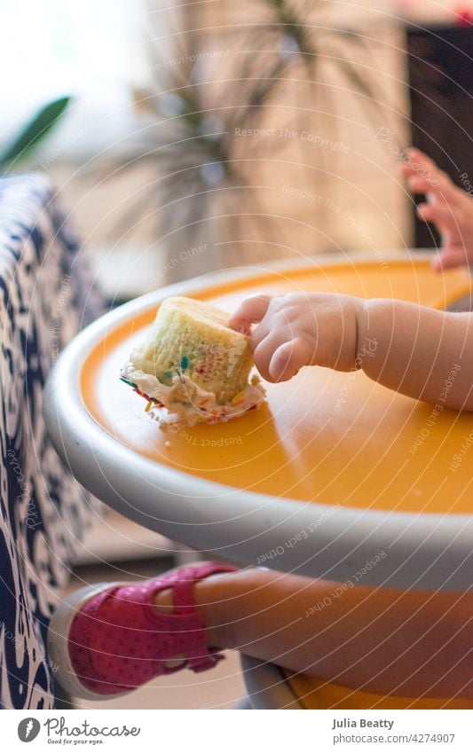 First birthday/first cake: one year old baby reaching out to overturned cupcake on high chair first birthday smash baby led weaning self feed 100 foods dessert