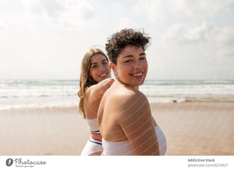 Smiling women in swimsuits on sandy beach near ocean sea girlfriend happy swimwear sky coast female young vacation harmony shore enjoy daytime together water