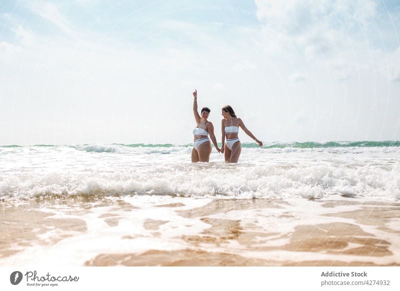 Ladies standing in sea near sandy coast women ocean friend having fun beach smile swimsuit blue sky happy female aqua holding hands seashore summertime young