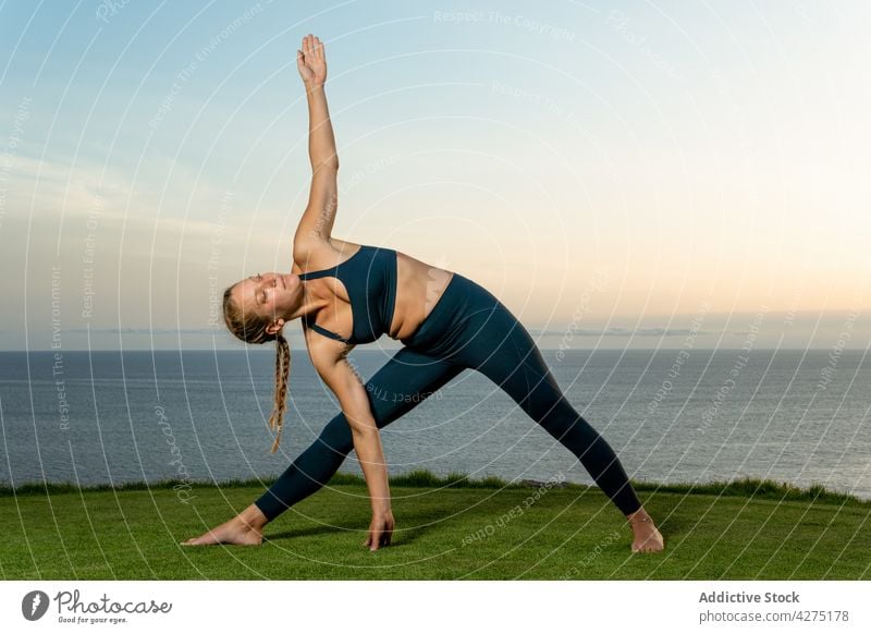 Woman performing triangle pose on sea shore woman yoga outstretch flexible triangle Pose wellness healthy lifestyle seashore Trikonasana evening grass practice