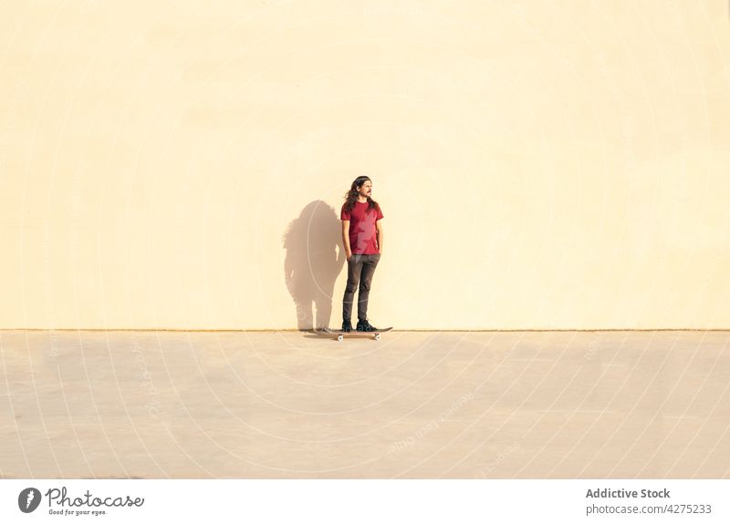 Skater on skateboard against wall with shadow outdoors skater hand in pocket sport contemplate lifestyle man solitude pavement admire shade walkway street stand