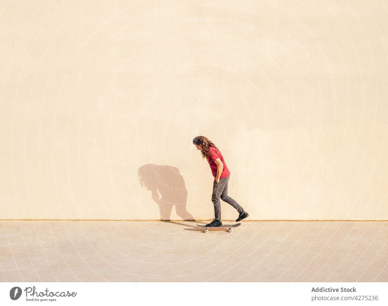 Skater on skateboard against wall with shadow outdoors skater hand in pocket sport contemplate lifestyle man solitude pavement admire shade walkway street stand